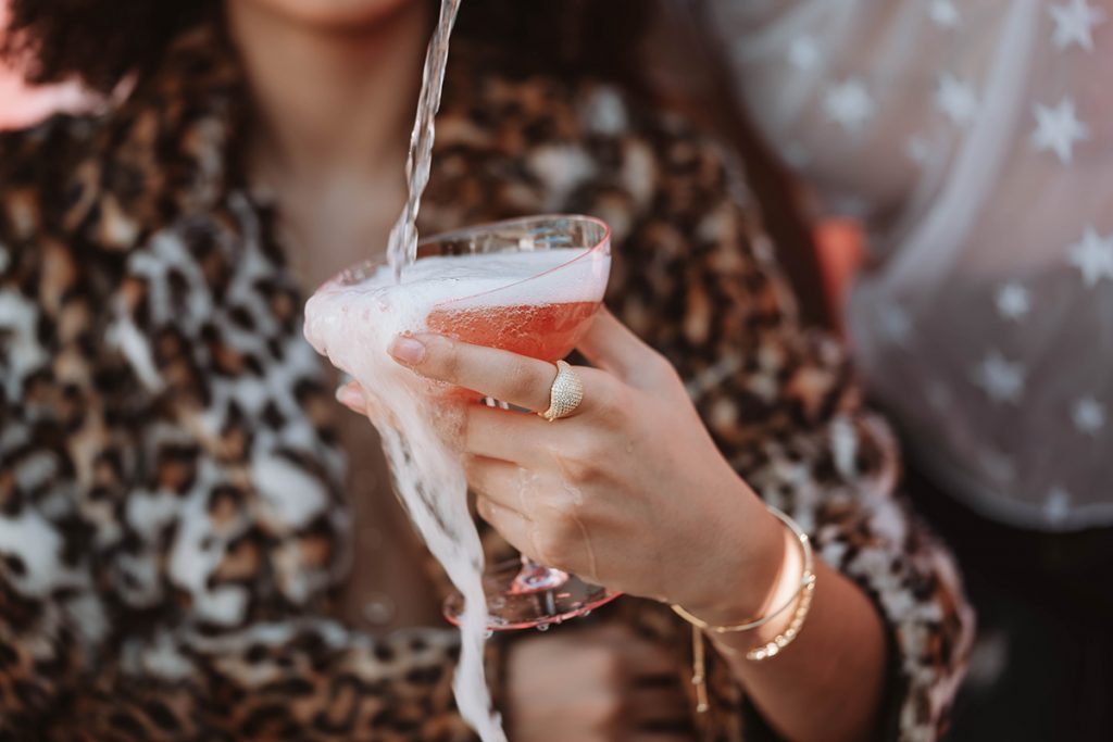 woman in a leopard print blouse holding a glass of sparkling rose wine that someone out of frame is pouring into