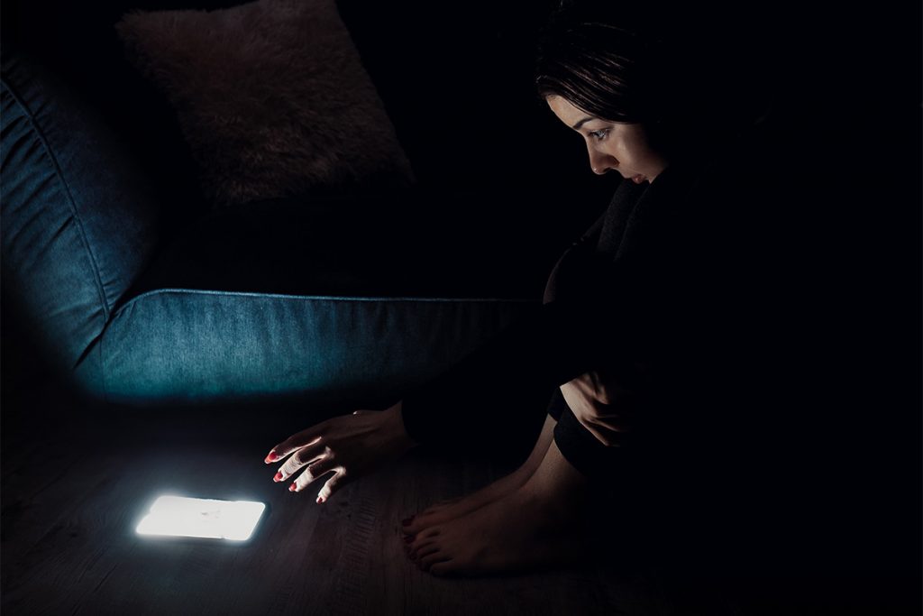 Woman reaching toward a lit cell phone in the dark