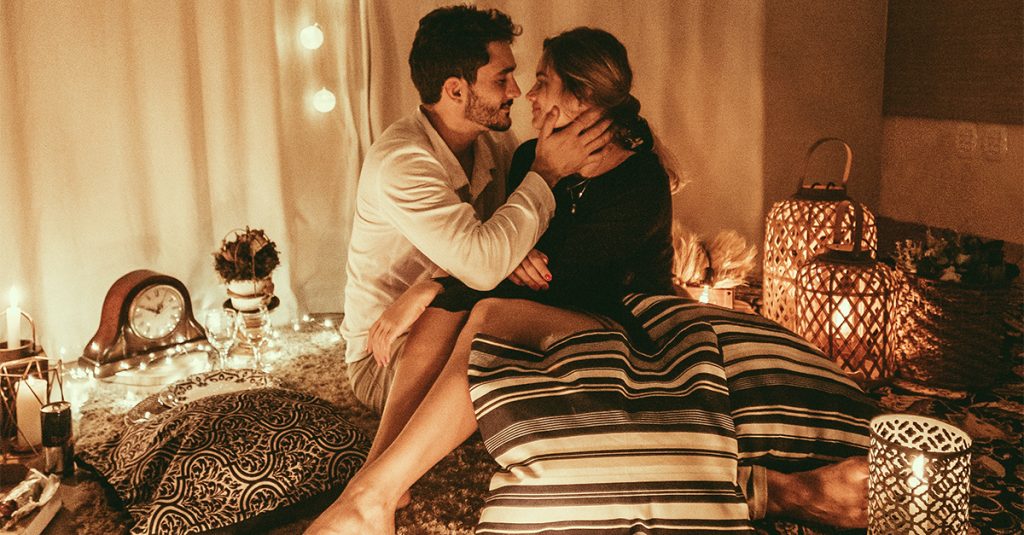 man and woman sitting on floor and about to kiss with lighted candles inside room